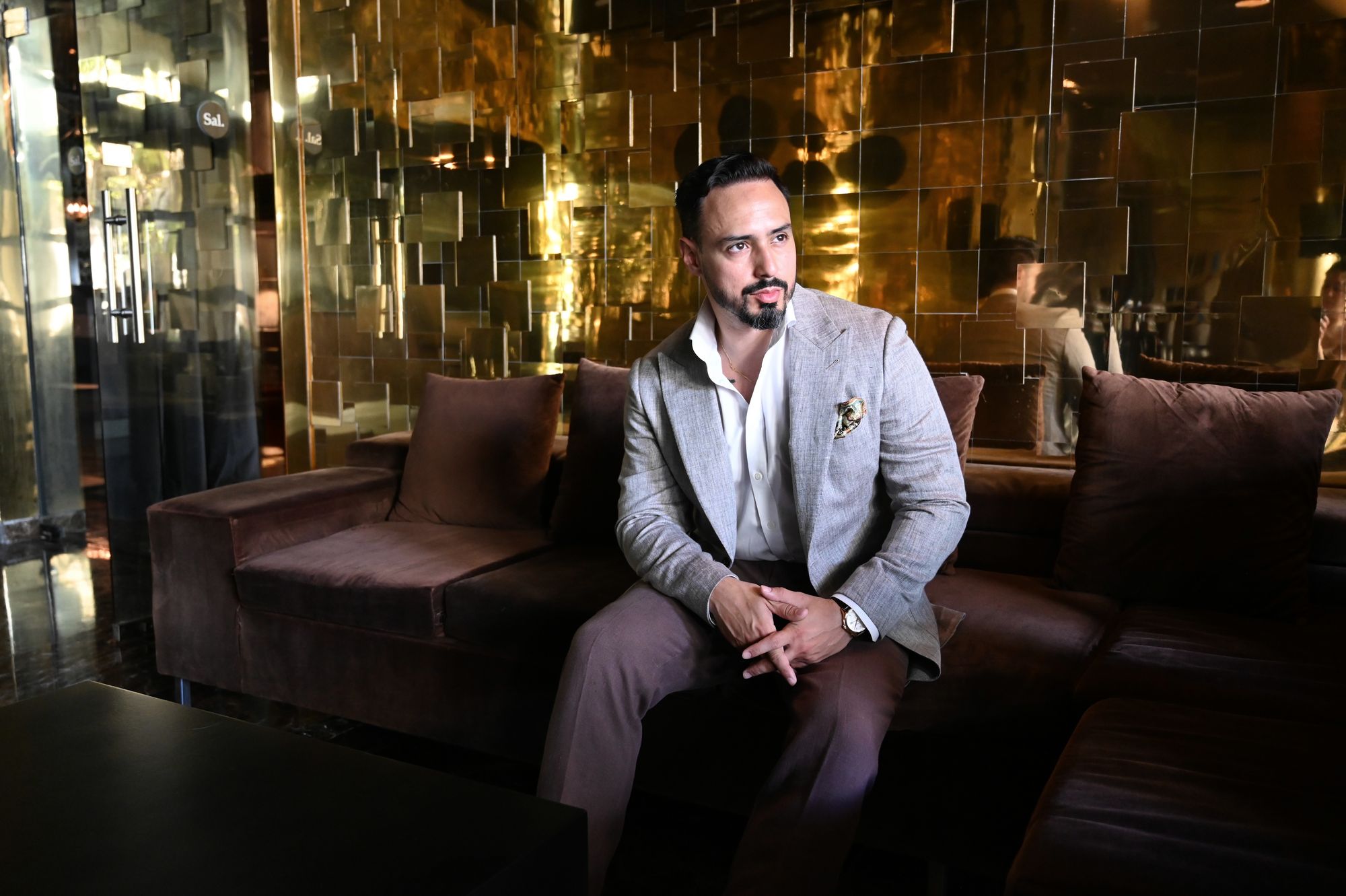 César seated in a leather lounge in a grey jacket